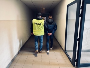 zdjęcie przedstawia policjanta prowadzącego zatrzymanego korytarzem rudzkiej komendy