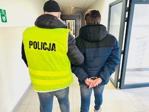 zdjęcie przedstawia policjanta prowadzącego zatrzymanego korytarzem rudzkiej komendy