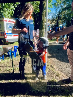 Policjantka pomaga trzymać dziecku policyjna tarczę