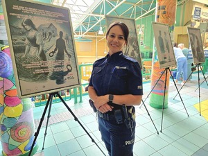 zdjęcie przedstawia policjantkę stojącą przed plakatami wystawy