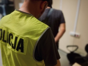 Policjant w odblaskowej kamizelce z napisem policja z osoba zatrzymaną