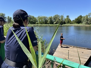 zdjęcie przedstawia policjantów przypatrujących się chłopcu na pomoście przy stawie