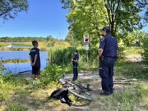 zdjęcie przedstawia policjantów w trakcie kontroli stawu, gdy rozmawiali z chłopcem, który przyjechał nad staw na rowerze