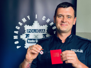 zdjęcie przedstawia policjanta z odznaką i legitymmacją