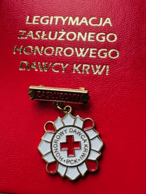 zdjęcie przedstawia odznakę honorowego dawcy krwi na tle legitymacji