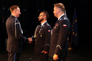 zdjęcie z uroczystości Święta Policji przedstawia moment gratulacji składanych przez Komendanta Miejskiego odznaczonemu policjantowi, obok stoi Xastępca Komendanta Wojewódzkiego