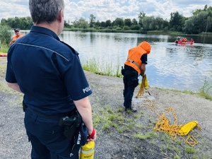 zdjęcie przedstawia ćwiczenia z ratownictwa wodnego, jeden z policjantów rzuca rzutkę do wody, a drugi stoi asekuracyjnie za nim