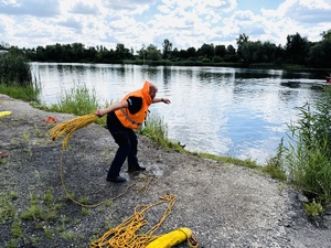 zdjęcie przedstawia ćwiczenia z ratownictwa wodnego gdy policjant rzuca rzutką ratowniczą do wody w kierunku pozoranta