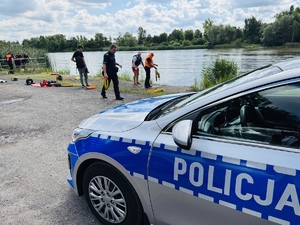 zdjęcie przedstawia ćwiczenia z ratownictwa wodnego - widać radiowóz policyjny i ćwiczących policjantów pod okiem instruktora - ratownika