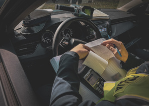 zdjęcie poglądowe - policjant w radiowozie wypisuje dokumentację