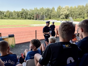 Policjanci prowadzą rozmowę, dzieci siedzą na trybunach