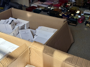 Na zdjęciu w kartonie znajdują się opakowania perfum, w tle rozłożone perfumy