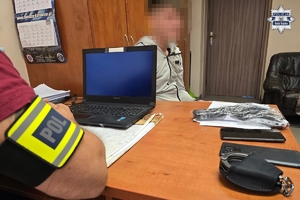zdjęcie przedstawia policjanta przy biurku i siedzącego po drugiej stronie zatrzymanego