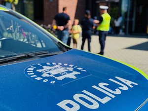 zdjęcie przedstawia policyjny radiowóz i policjanta z policjantką przy wejściu do szkoły