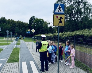 Zdjęcie przedstawia policjanta ruchu drogowego z dziećmi w miasteczku ruchu drogowego