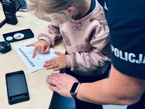 zdjęcie przedstawia przedszkolaka, który na specjalnej kartce odbija swoje linie papilarne z pomocą policjantki