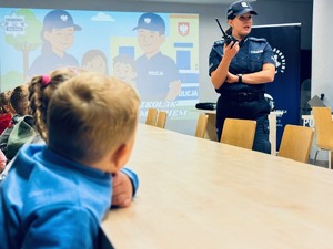 zdjęcie przedstawia przedszkolaków na sali gdzie policjantka pokazuje im swoją pracę
