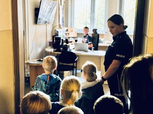 zdjęcie przedstawia przedszkolaków przedszkolaki wraz z policjantką zapoznają się z pracą dyżurnych