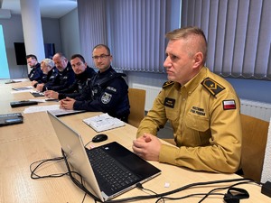 zdjęcie przedstawia strażaka przedstawiającego przepisy pożarowe, obok widać siedzących policjantów uczestniczących w ćwiczeniach