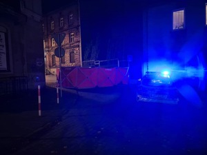 zdjęcie przedstawia miejsce wypadku z czerwonym parawanem zasłaniającym zwłoki pieszego i policyjnym radiowozem z włączonymi światłami błyskowymi