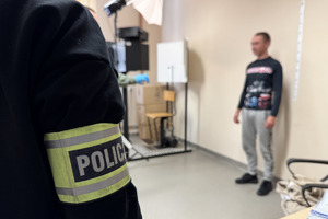 zdjęcie przedstawia policjanta i zatrzymanego, któremu technik wykonuje zdjęcia do akt
