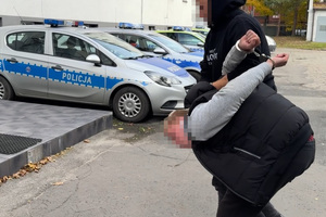 zdjęcie przedstawia policjanta kryminalnego prowadzącego sprawcę w kajdankach do komendy