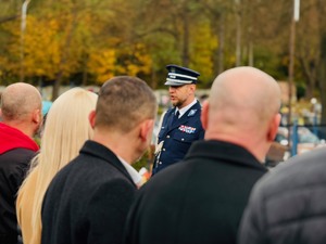 zdjęcie przedstawia policjantów pracujących wraz ze zmarłym oraz przemawiającego komendanta