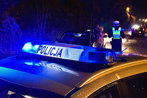 zdjęcie przedstawia policjantów stojących przy kontrolowanym samochodzie, na pierwszym planie dach radiowozu z policyjnymi kogutami