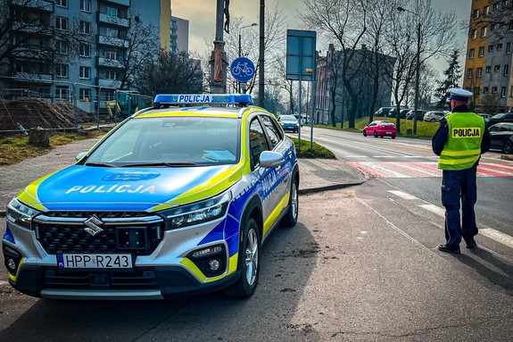 zdjęcie przedstawia policjanta z drogówki i radiowóz na jeden z ulic miasta