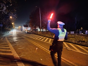 zdjęcie policjanta z drogówki zatrzymującego nocą nadjeżdżający pojazd przy pomocy latarki