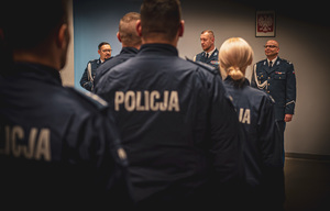 zdjęcie przedstawia miejsce uroczystej zbiórki w trakcie której policjanci stoją słuchając przemówienia komendanta