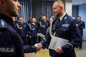 zdjęcie przedstawia miejsce uroczystej zbiórki w trakcie której komendant gratuluje policjantowi