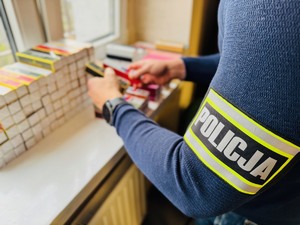 policjant trzymający podrobione perfumy w rękach, obok widać leżące sztaple podróbek