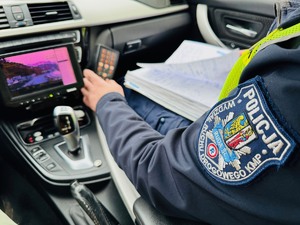 zdjęcie przedstawia wnętrze policyjnego radiowozu z wideorejestratorem i siedzącego policjanta z drogówki