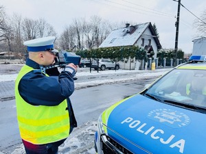 zdjęcie przedstawia policjanta z drogówki przy radiowozie gdy dokonuje pomiaru prędkości ręcznym miernikiem laserowym