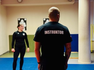 zdjęcie z zajęć na sali ćwiczeń rudzkiej komendy, widoczni na nich instruktor i uczestniczące kobiety