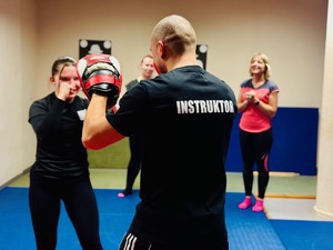 zdjęcie z zajęć na sali ćwiczeń rudzkiej komendy, widoczni na nich instruktor i uczestniczące kobiety