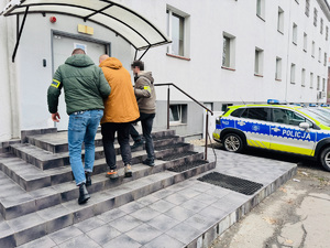 zdjęcie przedstawia policjantów kryminalnych prowadzących zatrzymanego z parkingu do komendy