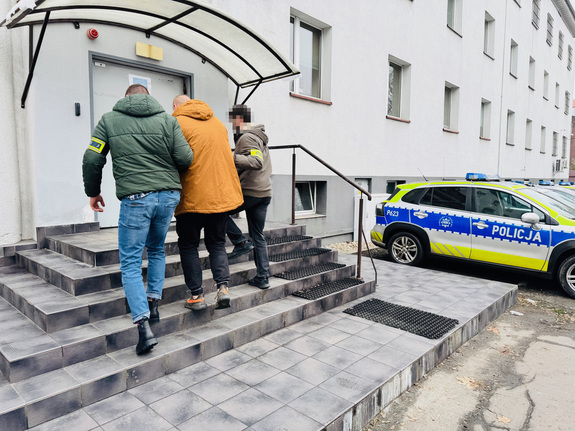 zdjęcie przedstawia policjantów kryminalnych prowadzących zatrzymanego z parkingu do komendy