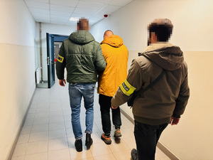 zdjęcie przedstawia policjantów kryminalnych prowadzących zatrzymanego korytarzem komendy