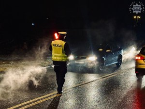 zdjęcie przedstawia policjanta z drogówki zatrzymującego samochód z włączonymi światłami