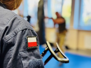 zdjęcie przedstawia ucznia klasy mundurowej trzymającego karabinek i policyjnego instruktora pokazującego kolejną postawę strzelecką