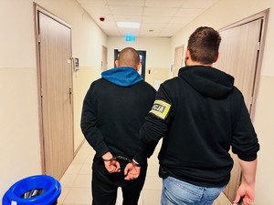 zdjęcie przedstawia policjanta prowadzącego zatrzymanego korytarzem komendy