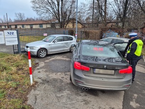 zdjęcie przedstawia dwa samochody, srebrny bmw przyparty do zamkniętej bramy wjazdowej i czarne bmw w którym wyświetla się napis police i obok stojącego policjanta z drogówki