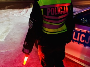 Zdjęcie przedstawia sylwetkę umundurowanego policjanta ruchu drogowego w kamizelce odblaskowej przy radiowozie