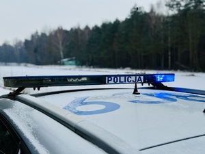 Zdjęcie przedstawia zbliżenie na światła uprzywilejowane radiowozu, w tle zbiornik wodny