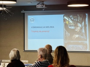 Seniorzy słuchają wykładu, w tle prezentacja