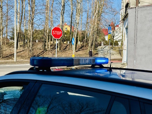 Zdjęcie przedstawia sygnały uprzywilejowane radiowozu, w tle osoba przechodzi przez przejście dla pieszych