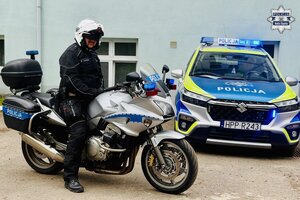 Policjant na motocyklu służbowym, w tle radiowóz