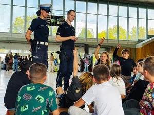 policjanci stojący na hali sportowej przed siedzącymi dziećmi